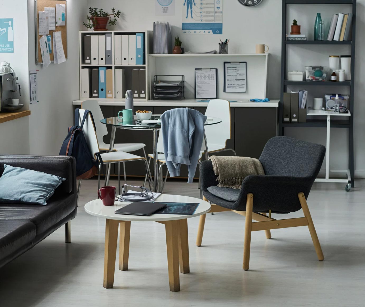 Modern office lounge with chairs, table, laptop, bookshelves, and casual items creating a cozy atmosphere.