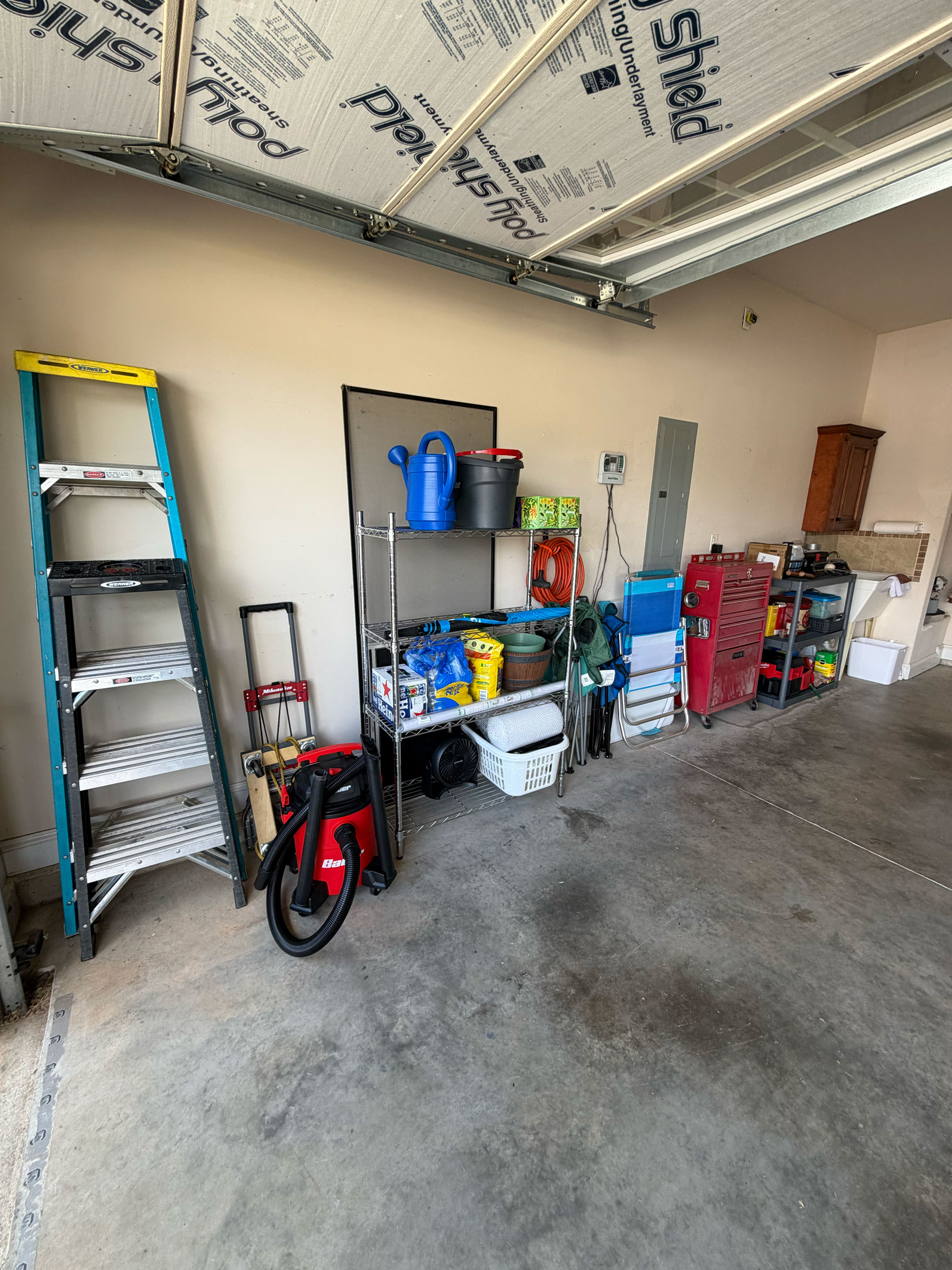 Organized garage with ladders, shelves of tools, bins, cleaning supplies, and a red tool chest.