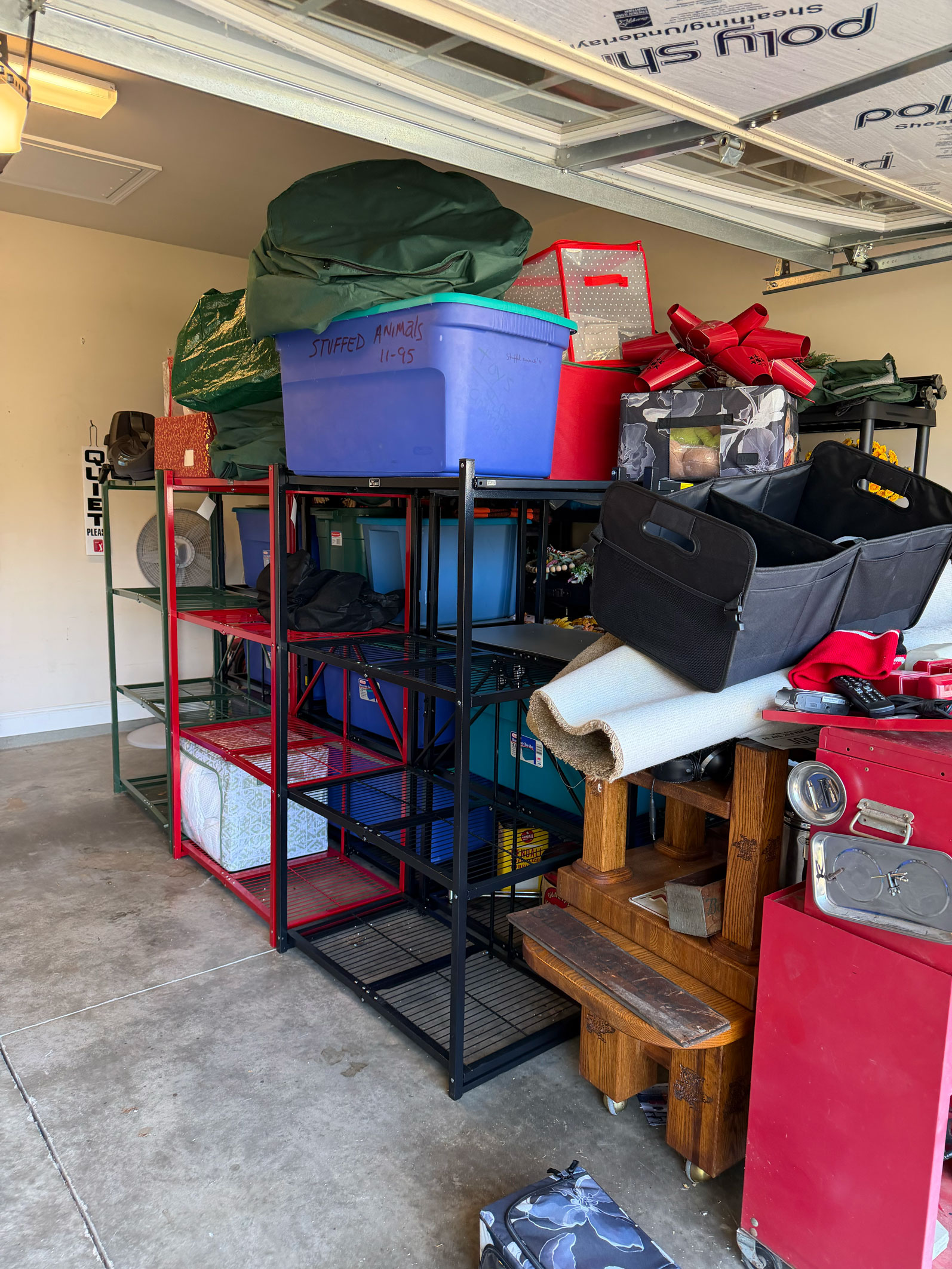 Shelves filled with bins, bags, and boxes in a garage, with rolled-up rugs and stored holiday items visible.