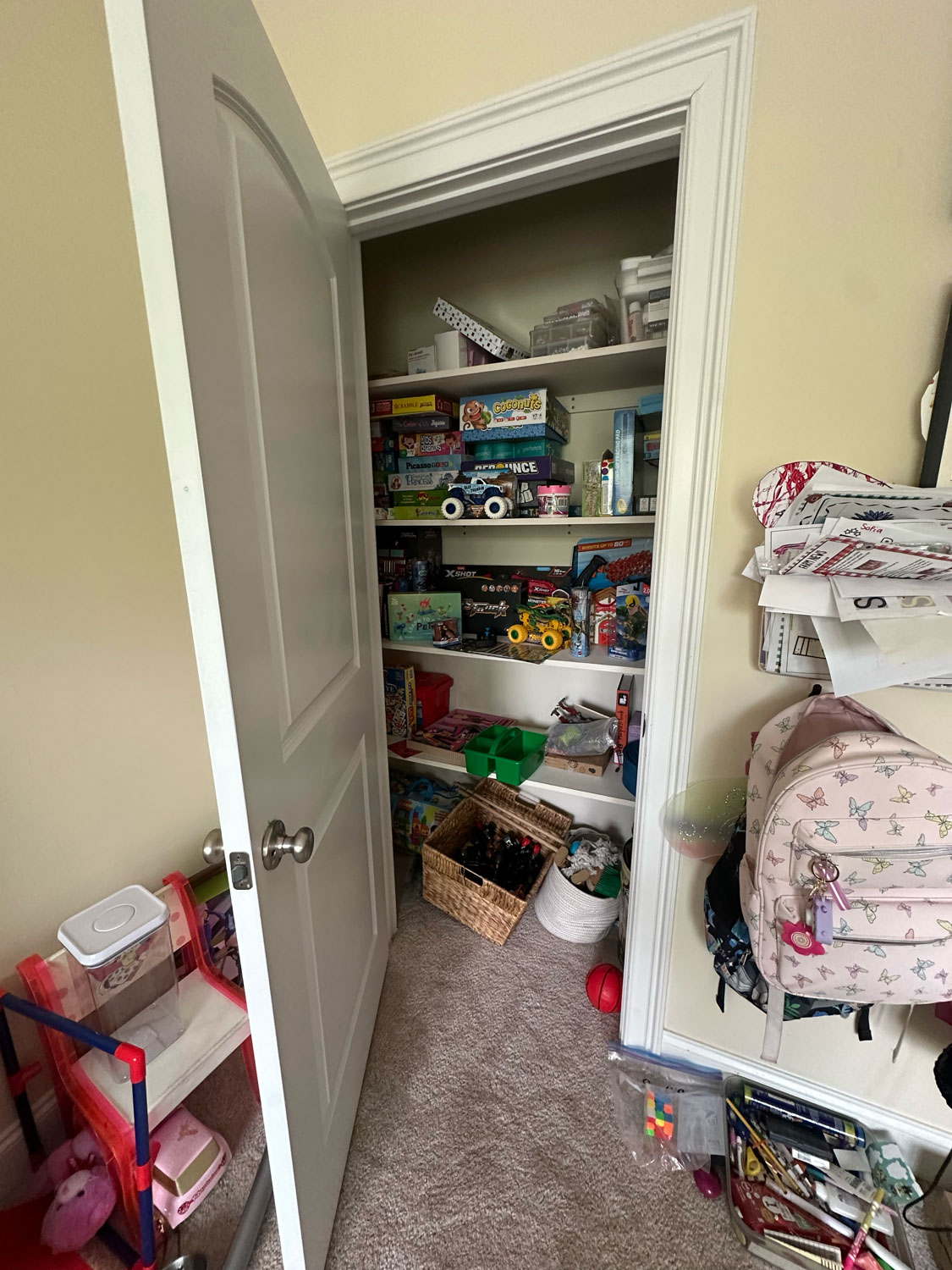 Open closet door reveals shelves filled with board games, toys, and a basket of figurines on the floor.