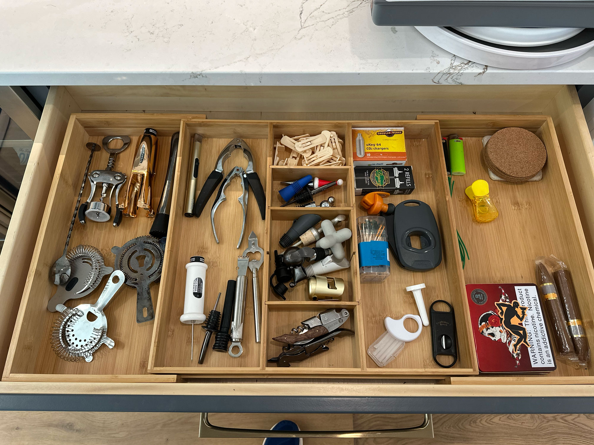 Drawer with various kitchen tools, gadgets, batteries, corks, matches, and small household items organized in sections.